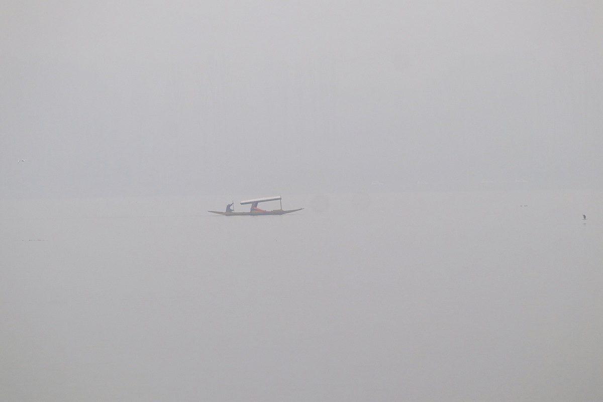 A man rows a boat on Dal lake during a misty winter morning