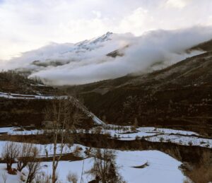 A scenic view of clouds hover over snow-clad hills after receiving fresh snowfall at Keylong