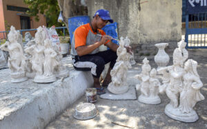 Artisan makes finish touch to idols of deity at roadside on hot summer day