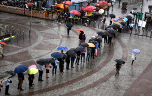 Commuters holding umbrellas stand in a queue as they wait for autorickshaw